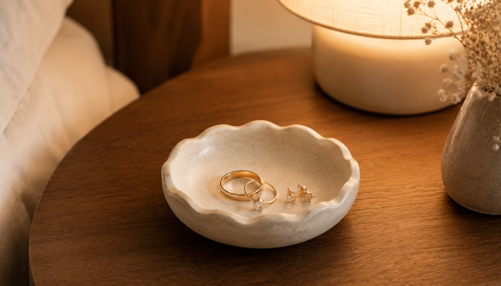 Handmade air dry clay ring dish in soft cream color sitting on a bedside table holding jewelry
