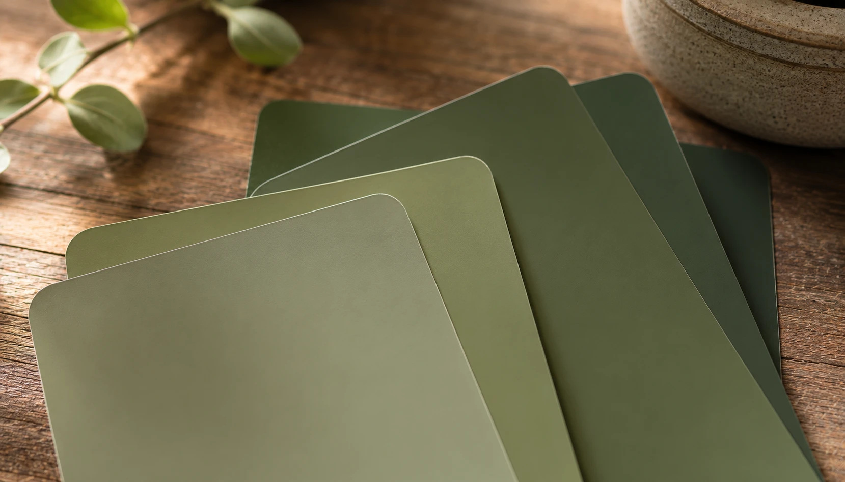Close up of olive green paint samples with different undertones held against a wood surface
